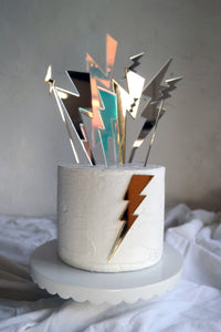 Multicoloured lightening bolts shaped cake topper on top of cake.
