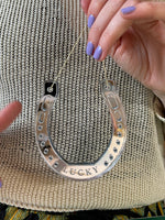 Load image into Gallery viewer, Hands with purple nail polish holding a horseshoe shaped ornament with the word lucky etched into it.

