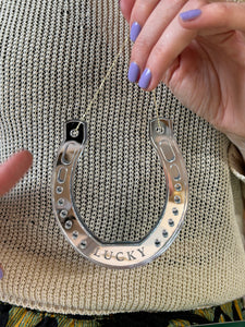 Hands with purple nail polish holding a horseshoe shaped ornament with the word lucky etched into it.