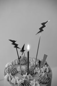 Lightening bolt shaped cake topper with candle on birthday cake.