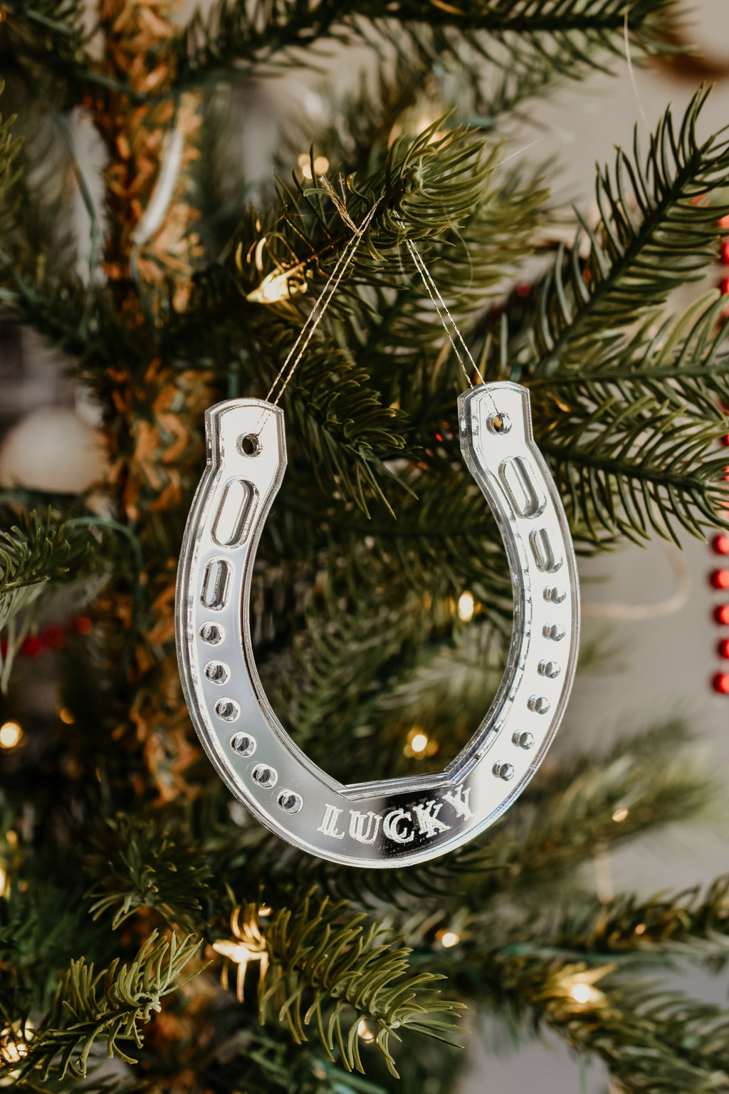 A horseshoe shaped ornament with the word Lucky hanging from a christmas tree.