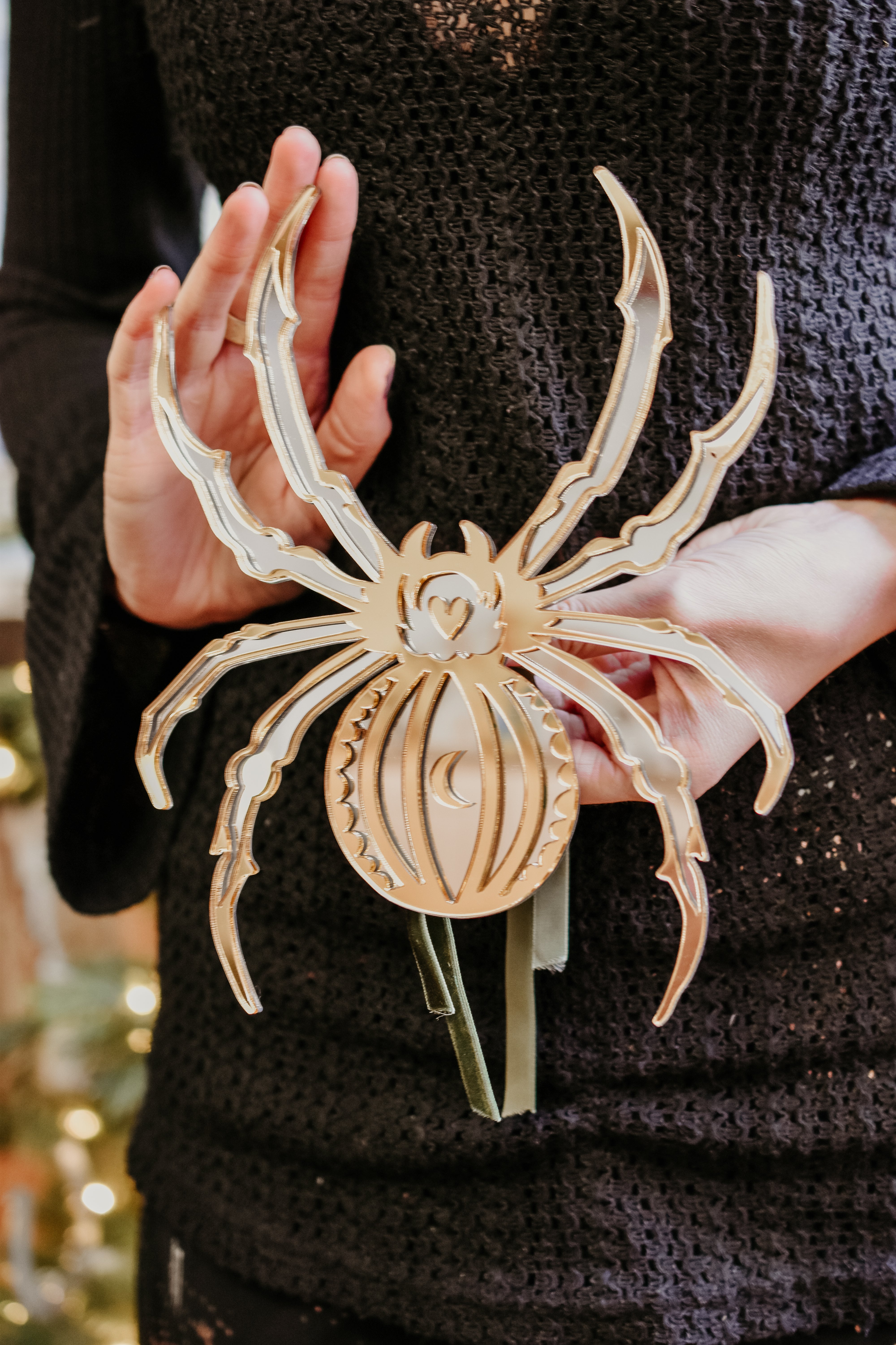 Hands holding a gold and silver spider shaped mirror that is a christmas tree topper.