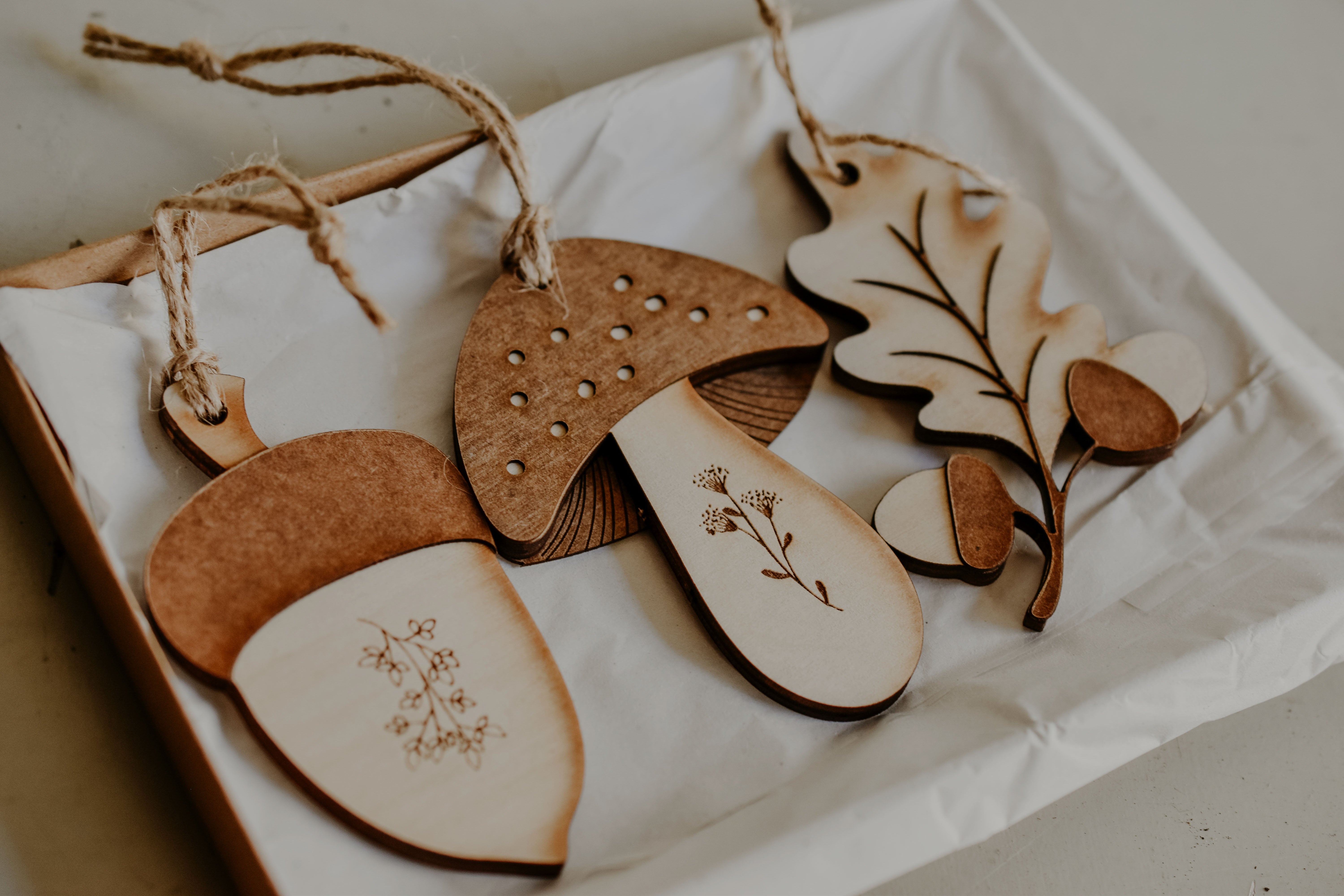 3 woodland themed decorations in the shape of a leaf, acorn and mushroom made from wood in a gift box.