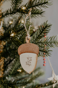 An acorn shaped wooden ornament hanging in a christmas tree.