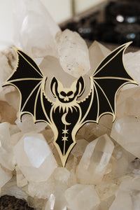 A black and gold bat shaped mirror lying on a bed of crystals