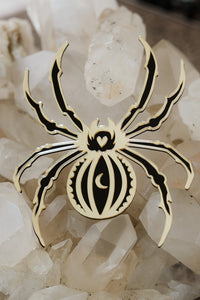 A black and gold spider mirror laying on a bed of crystals
