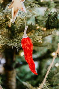 A chilli pepper shaped ornament hanging in a christmas tree.