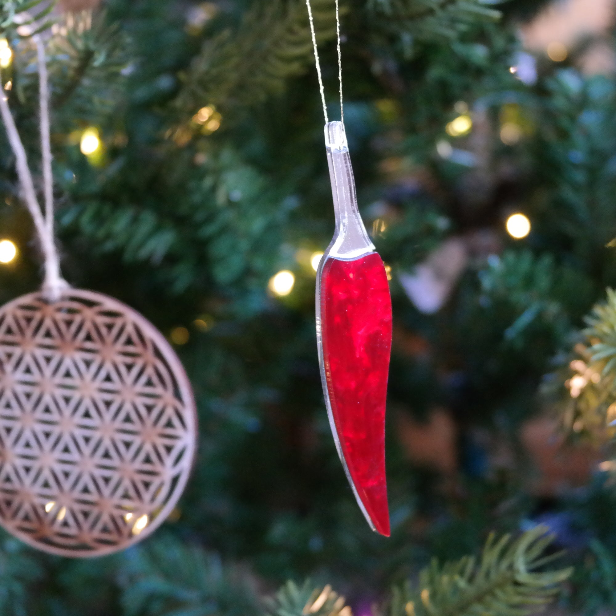 A chilli pepper shaped ornament hanging in a christmas tree with sparkling lights in the background.