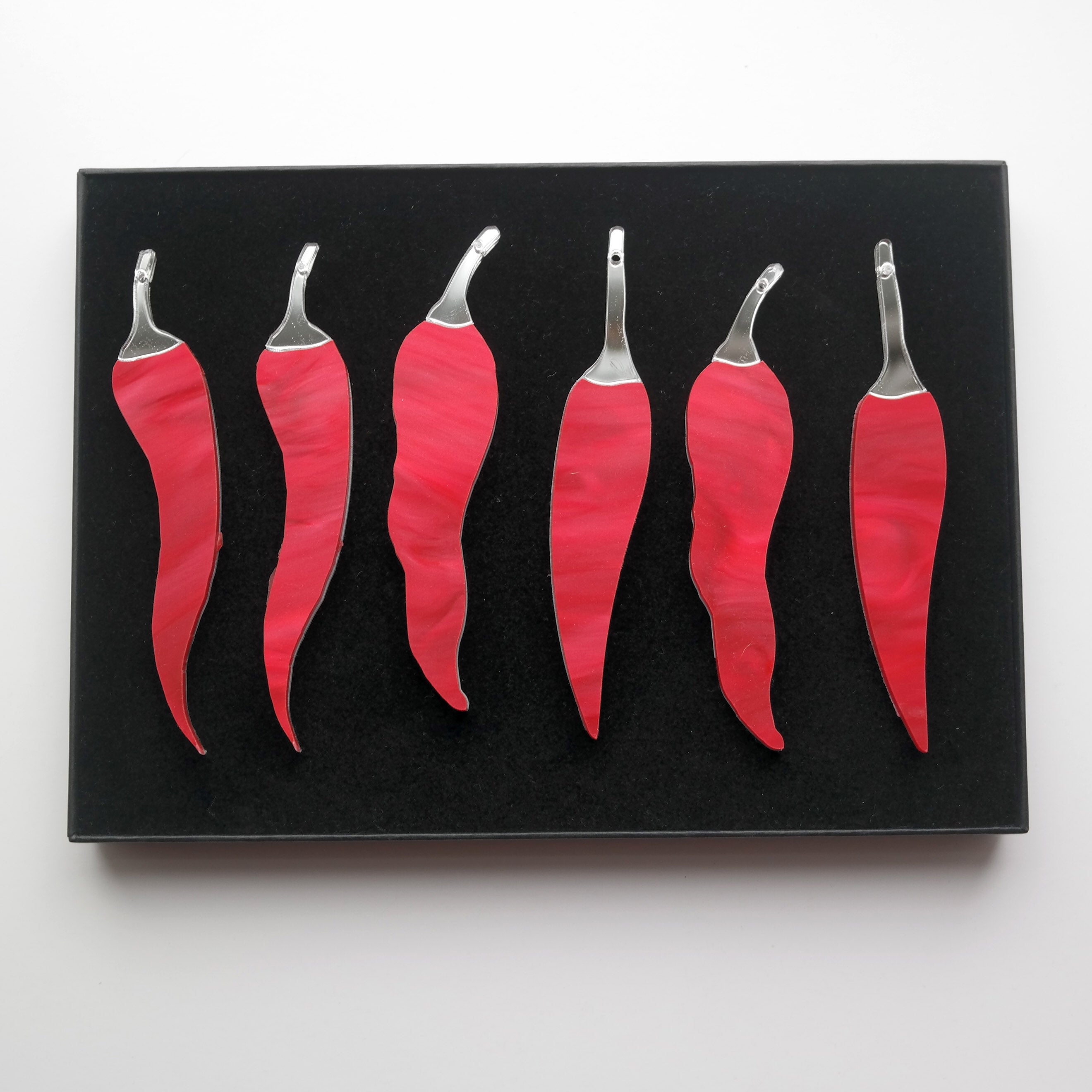 A photo taken from above of six chilli pepper shaped ornaments in a gift box.