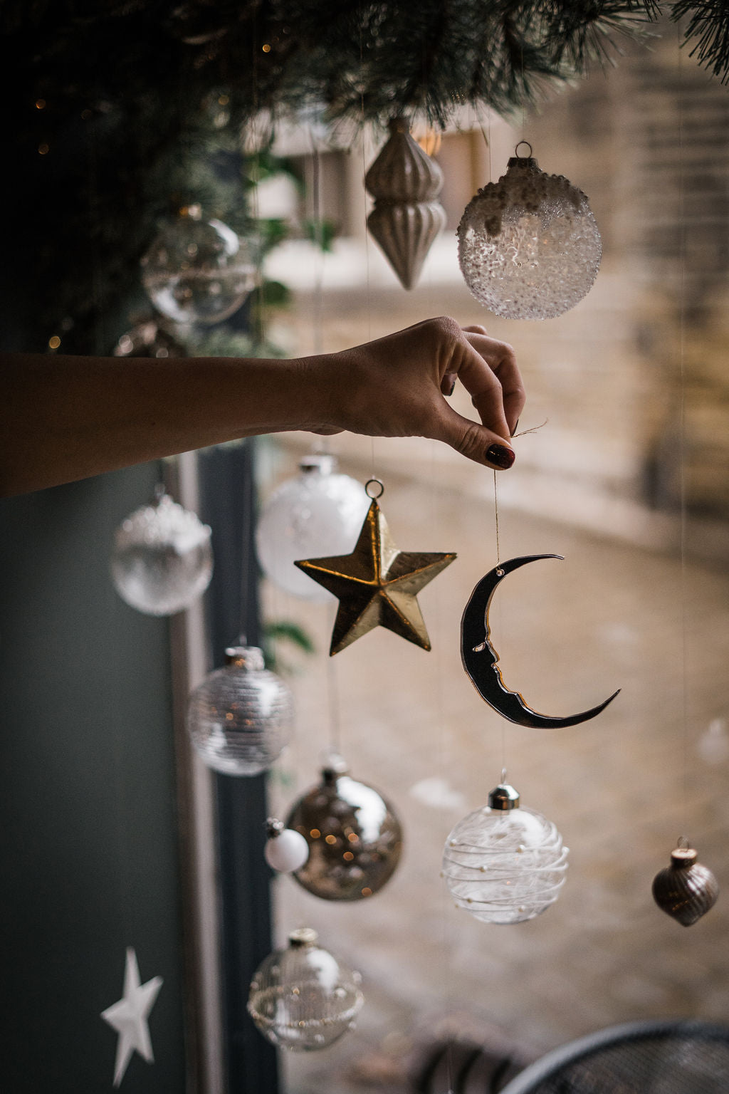 A crescent moon shaped bauble held in the window alongside christmas decorations