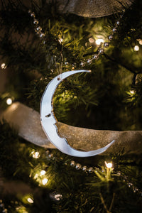 A crescent moon shaped bauble hanging in a christmas tree