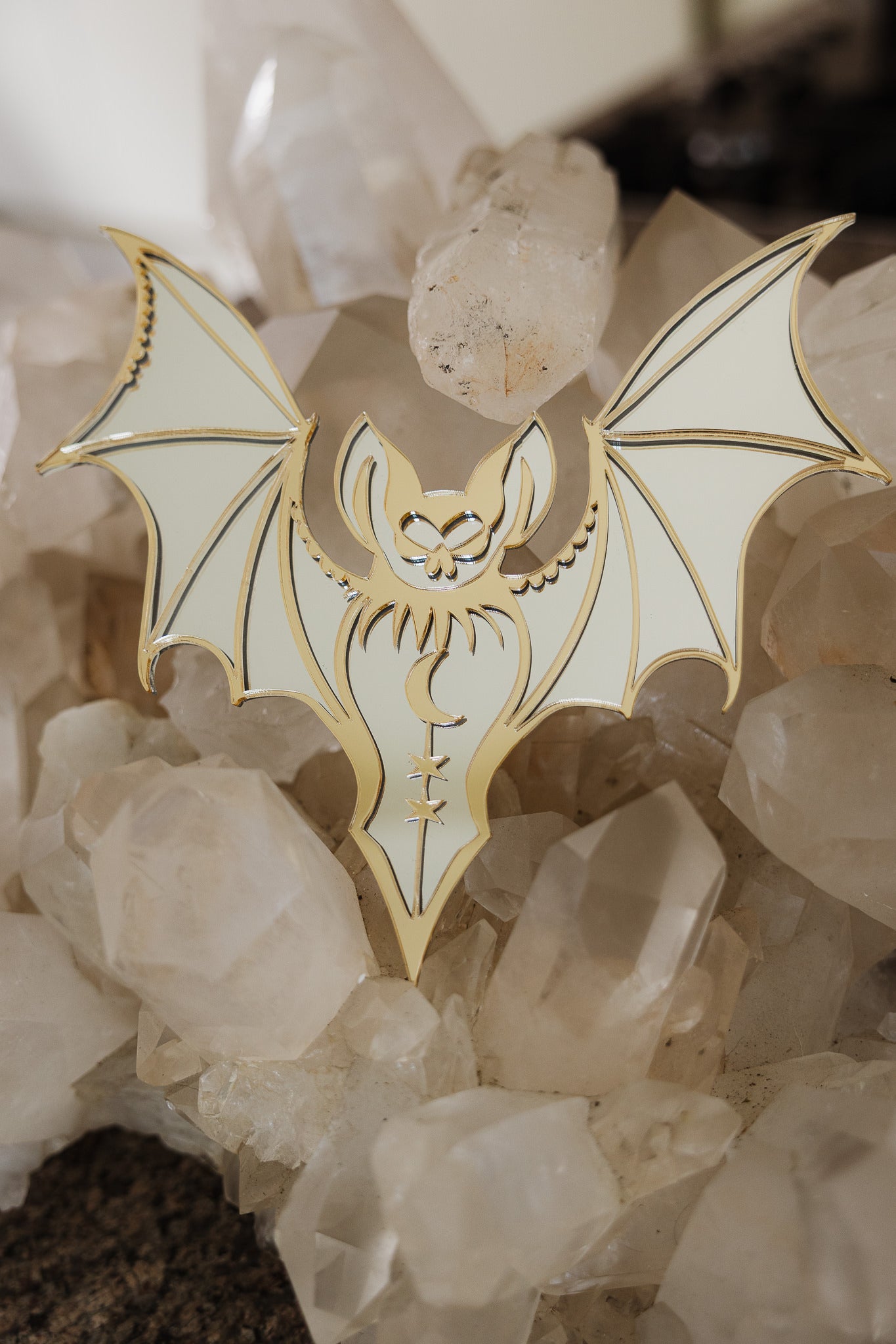 A gold bat shaped mirror laying on a bed of crystals
