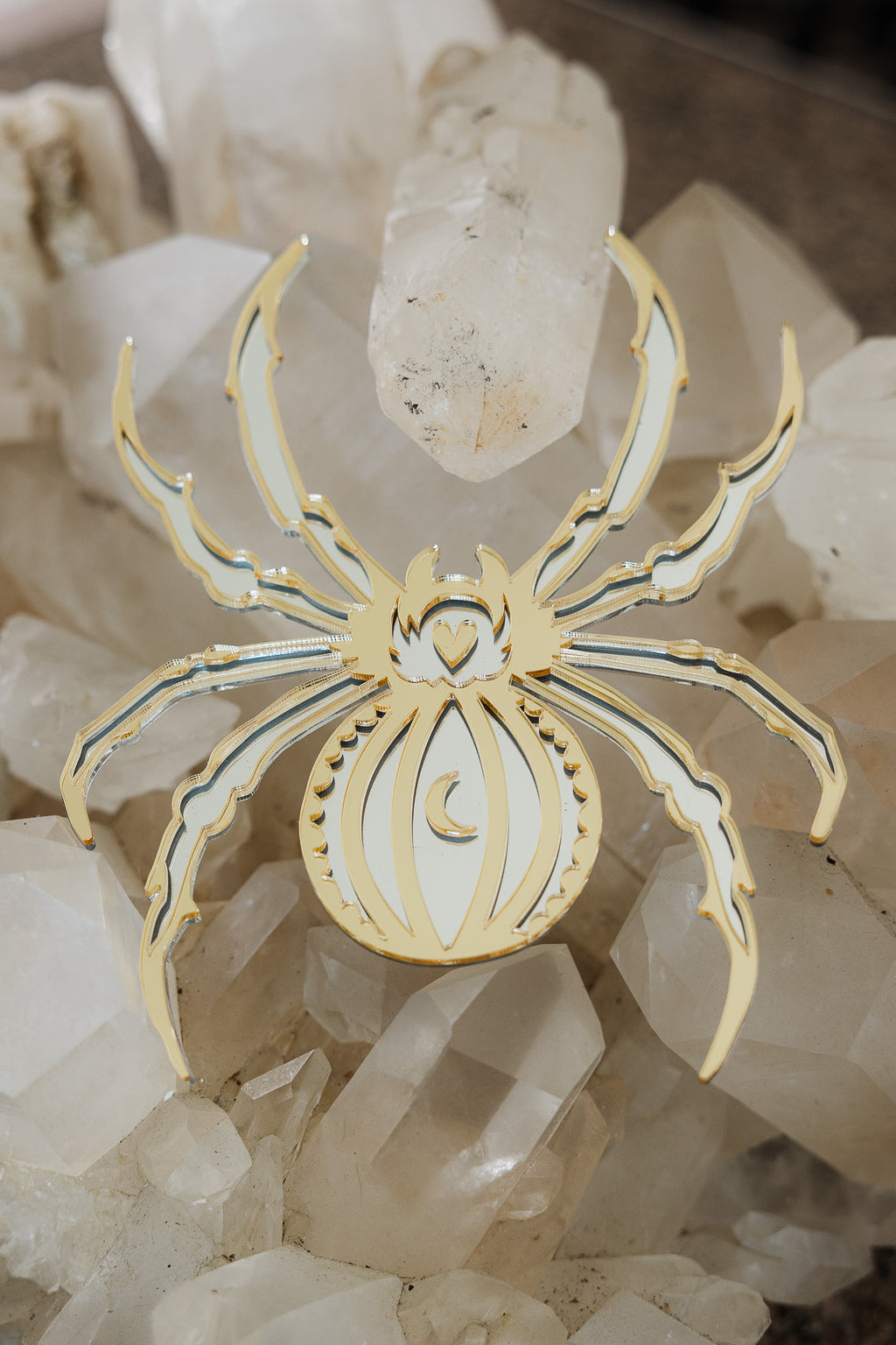 A gold spider shaped mirror laying on a bed of crystals