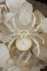 A gold spider shaped mirror laying on a bed of crystals