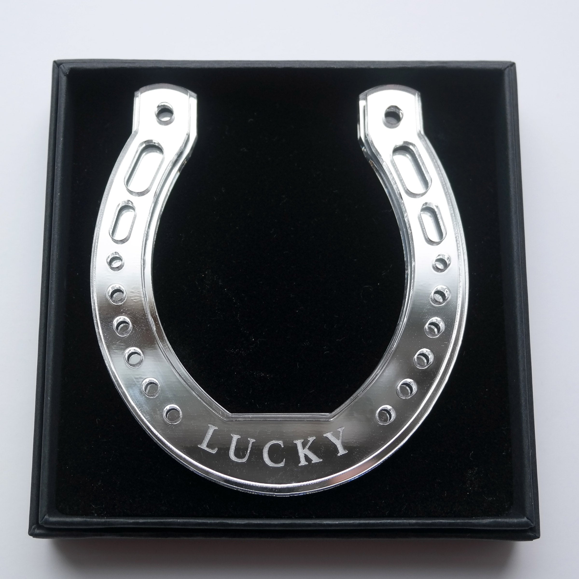 A silver horseshoe shaped ornament with the word lucky in a giftbox