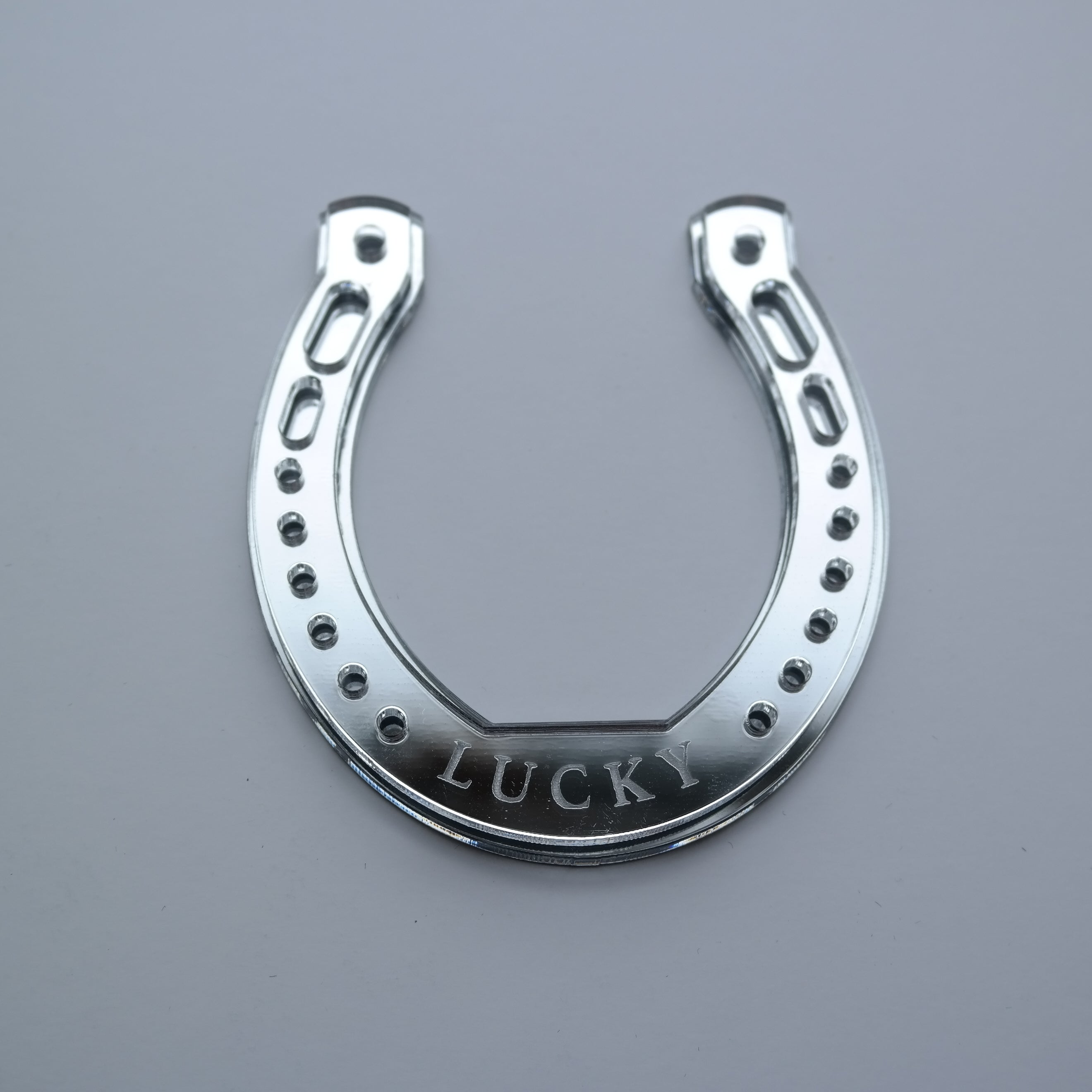 A horseshoe shaped ornament with the word lucky etched in, laying flat on a table.