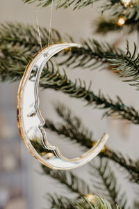 A handmade crescent moon shaped bauble ornament hanging in a tree