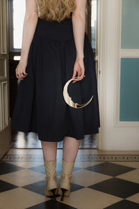 A crescent moon mirror held loosely behind a dress