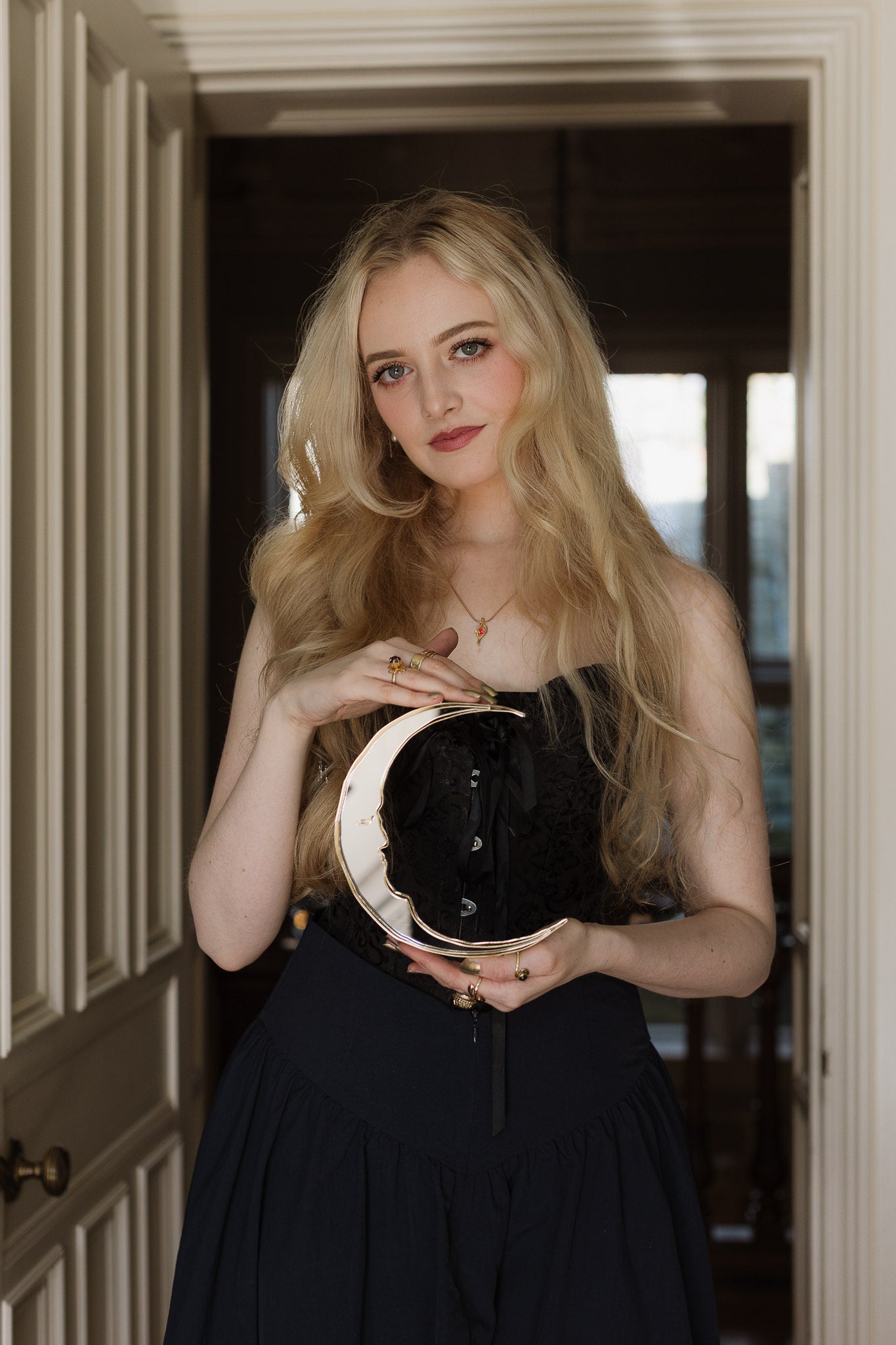 A gold crescent moon mirror held in the hands of a blonde woman