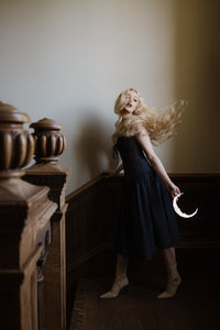 A gold crescent moon shaped mirror held in the hands of a blonde woman in the stairwell of an old manor house