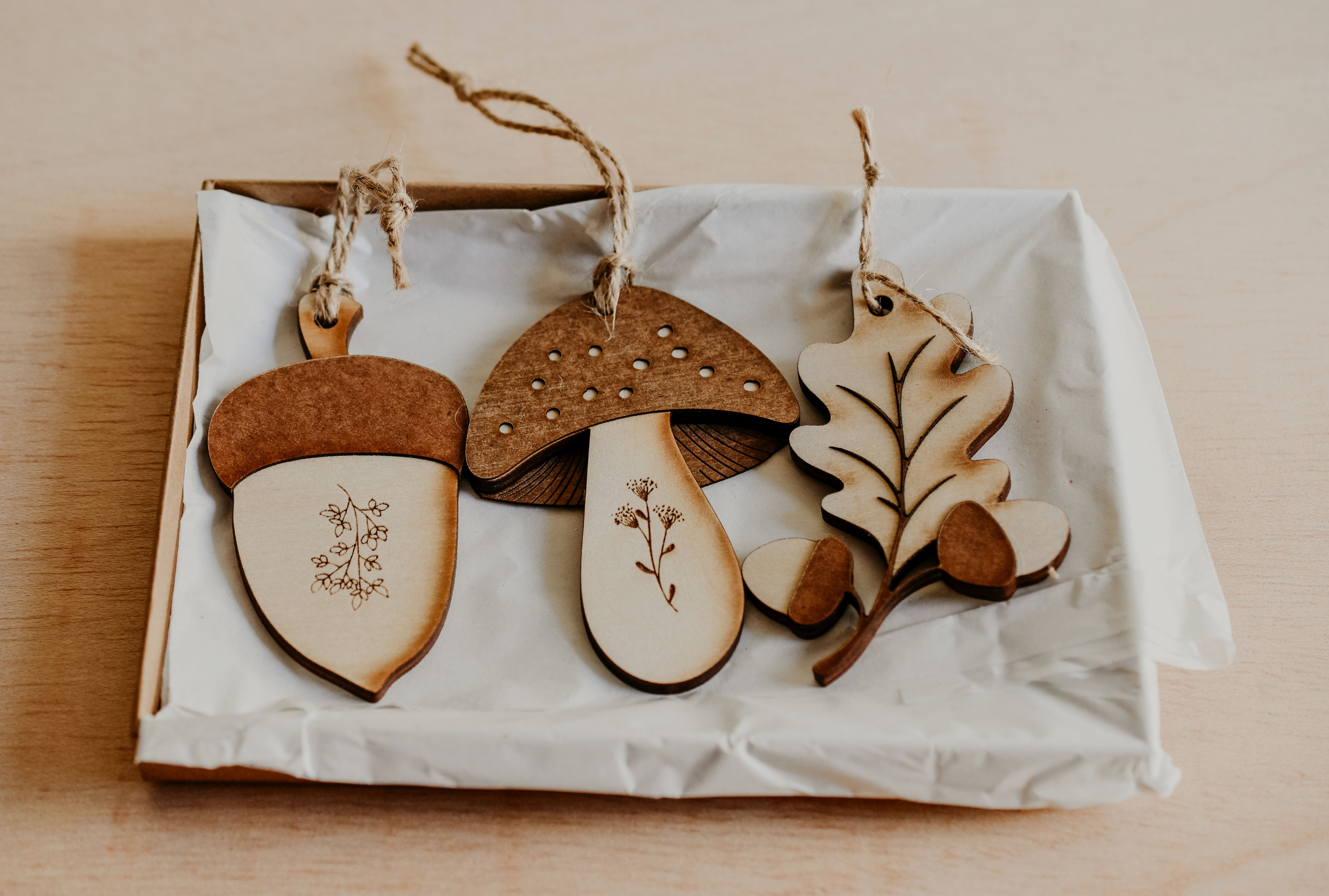 3 woodland themed decorations in the shape of a leaf, acorn and toadstool made from wood in a gift box.