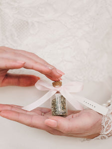 Wedding place name printed on pink bow attached to jar held in hands.