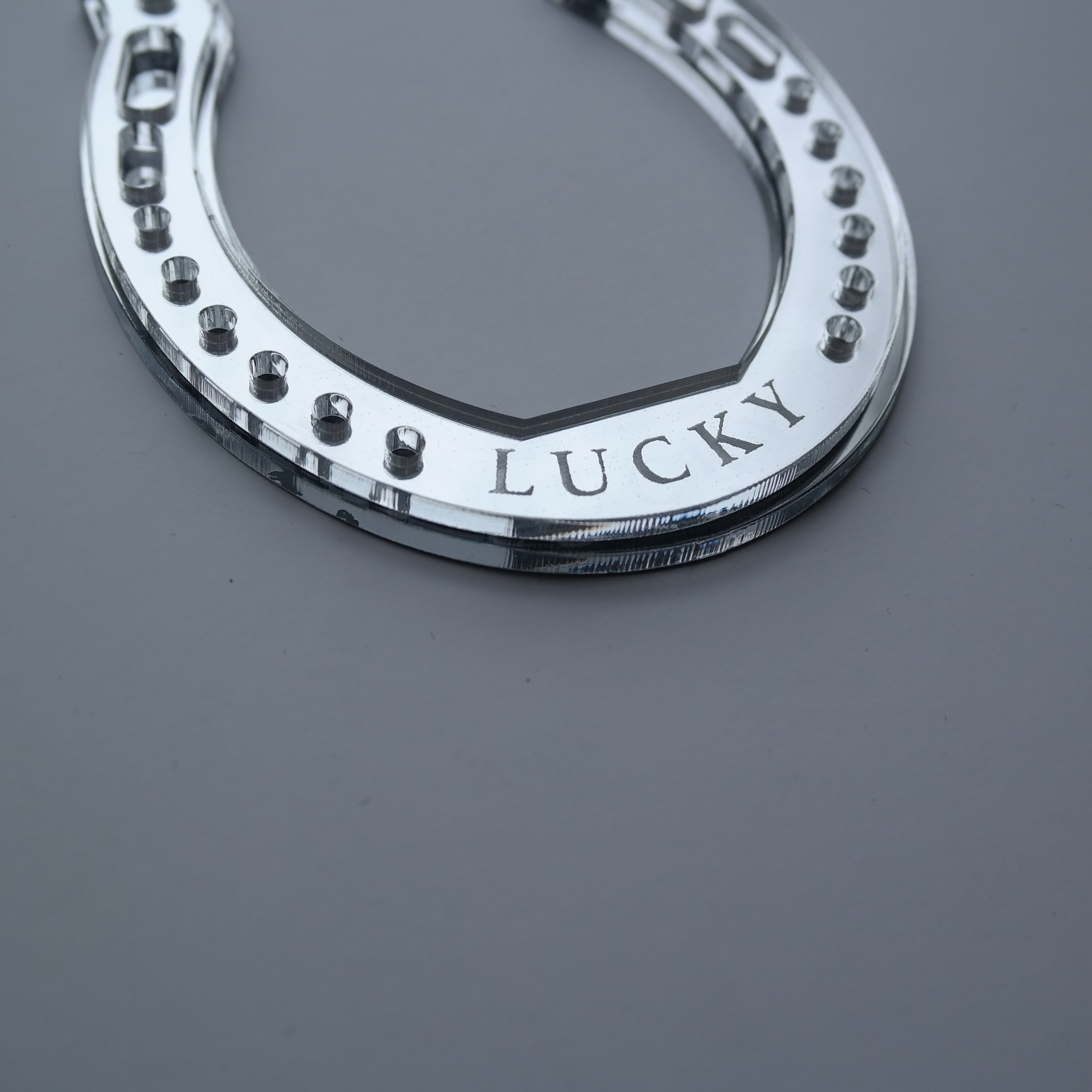A close up picture of a handmade silver horseshoe shaped ornament with the word lucky.