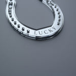 Load image into Gallery viewer, A close up picture of a handmade silver horseshoe shaped ornament with the word lucky.
