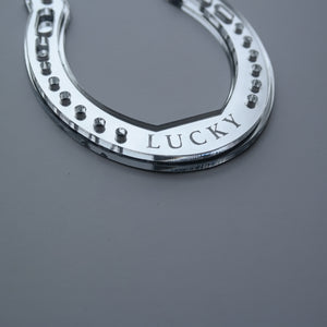 A close up picture of a handmade silver horseshoe shaped ornament with the word lucky.
