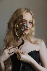 A blonde haired girl holding a engraved snake shaped mirror next to her face