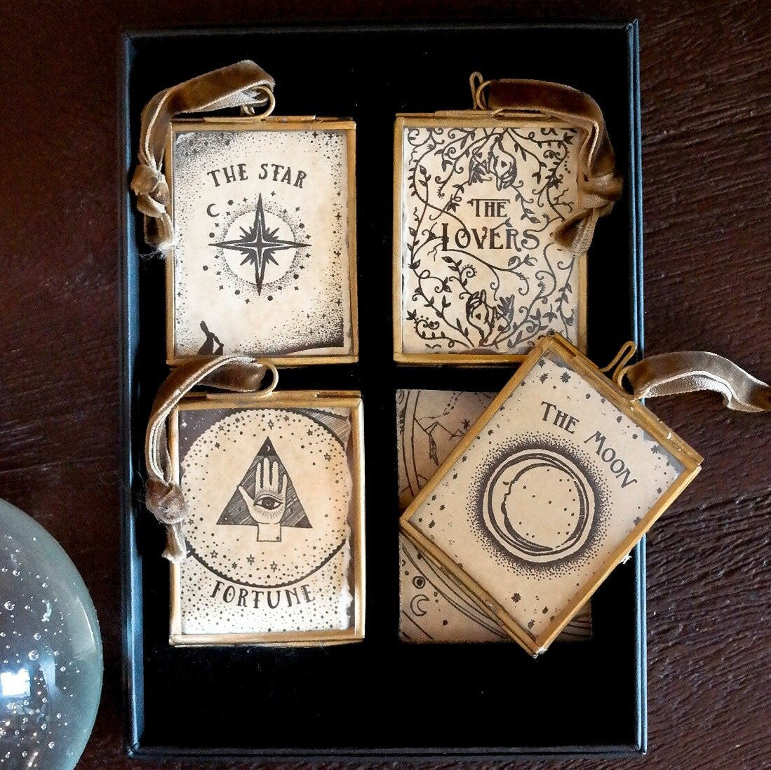 Four decorative ornaments labeled 'The Star', 'The Lovers', 'Fortune', and 'The Moon' in a black box on a wooden surface.