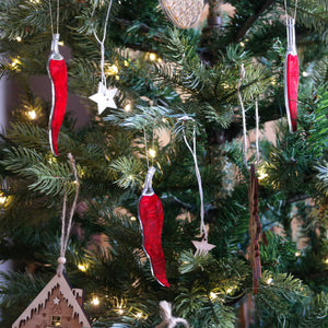 three chilli pepper shaped ornaments hanging in a christmas tree.