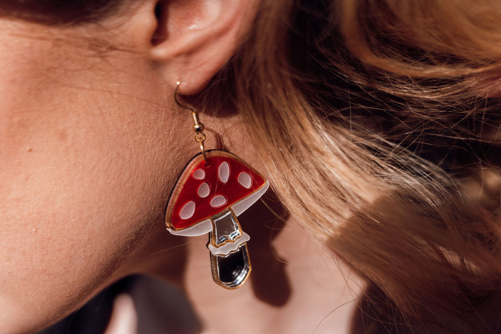 A red, white and silver toadstool shaped earring in ear handmade with acrylic and mirror.