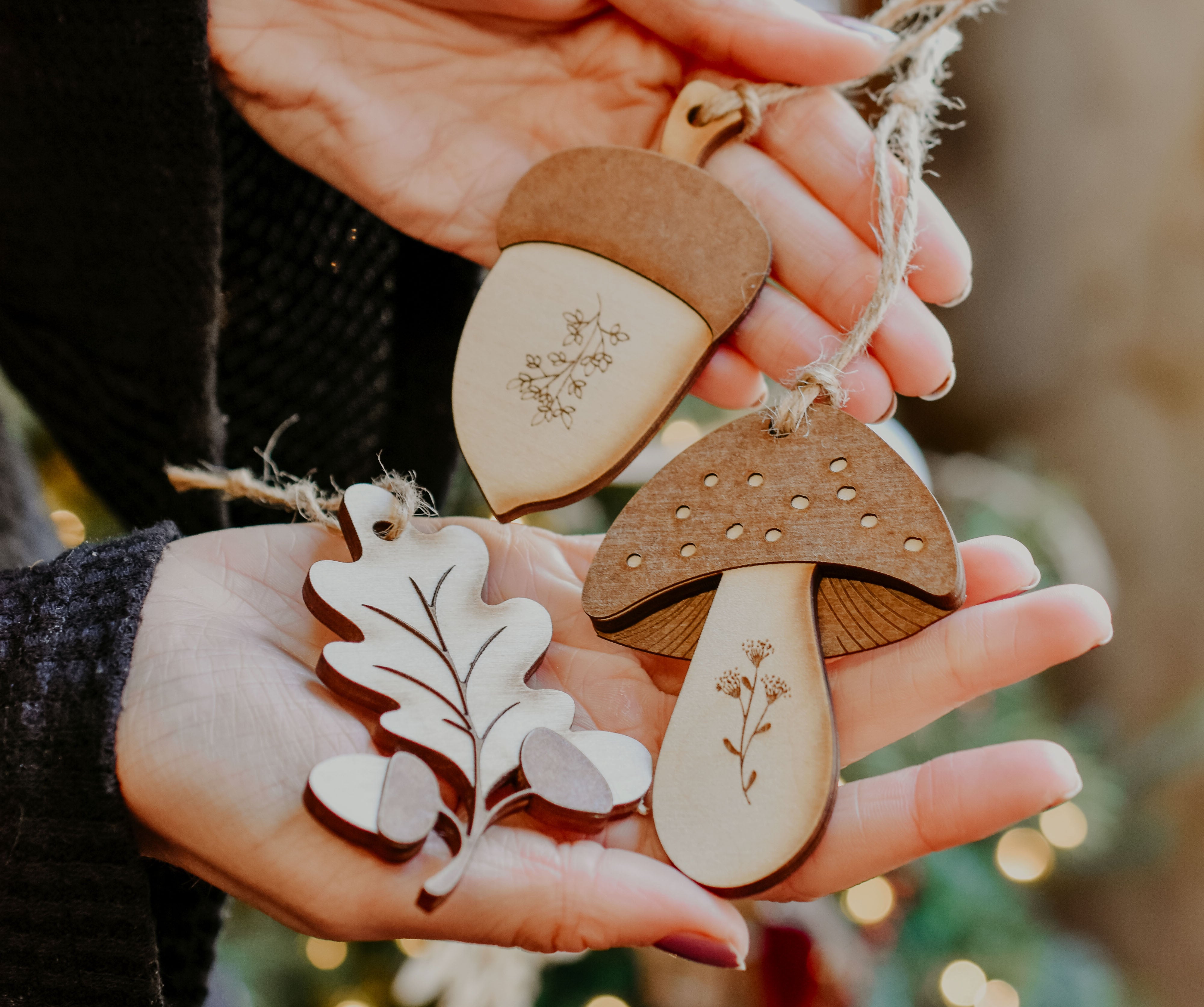 3 woodland themed decorations in the shape of a leaf, acorn and mushroom handmade from wood in a person's hands.