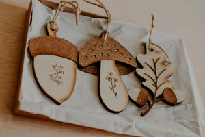 3 woodland themed decorations in the shape of a leaf, acorn and mushroom handmade from wood in a gift box.