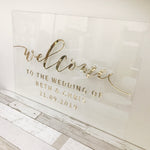 Load image into Gallery viewer, Clear acrylic wedding sign with welcome to the wedding with gold.
