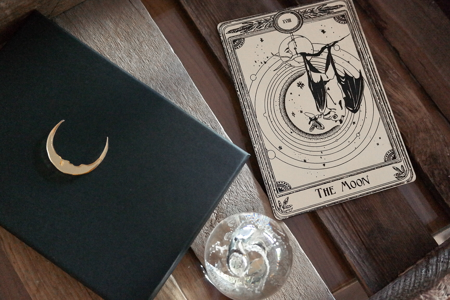 A decorative tarot card with a bat hanging under the moon next to gift box.