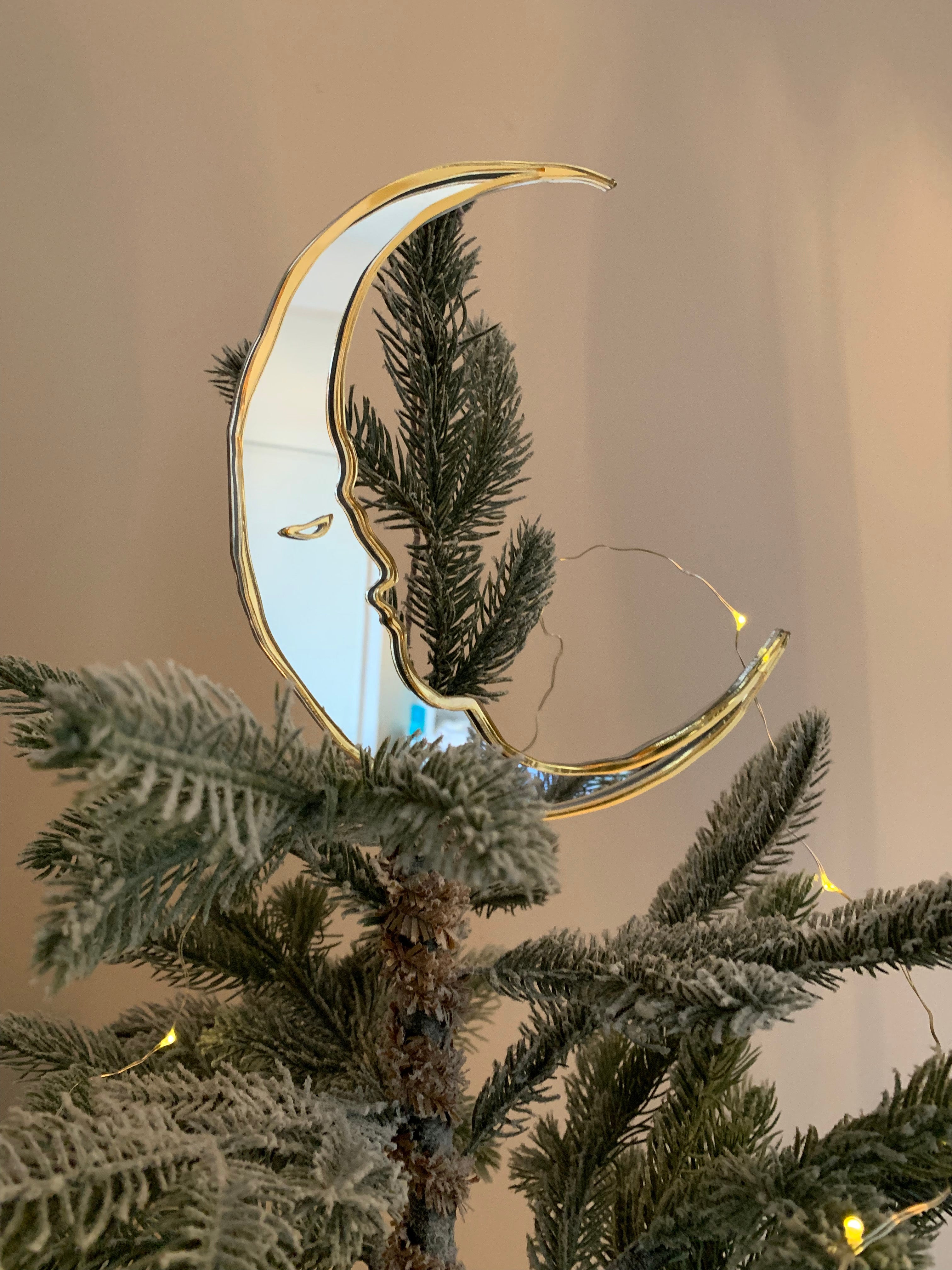 A crescent moon shaped christmas tree topper on the top of a christmas tree.