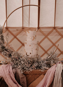 Gold star and crescent moon cake charms on white tiered wedding cake and floral display.