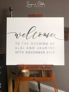 White acrylic wedding sign with welcome to the wedding in silver on wooden easel