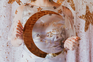 a clear acrylic wedding sign with gold names and gold crescent moon held in hands.