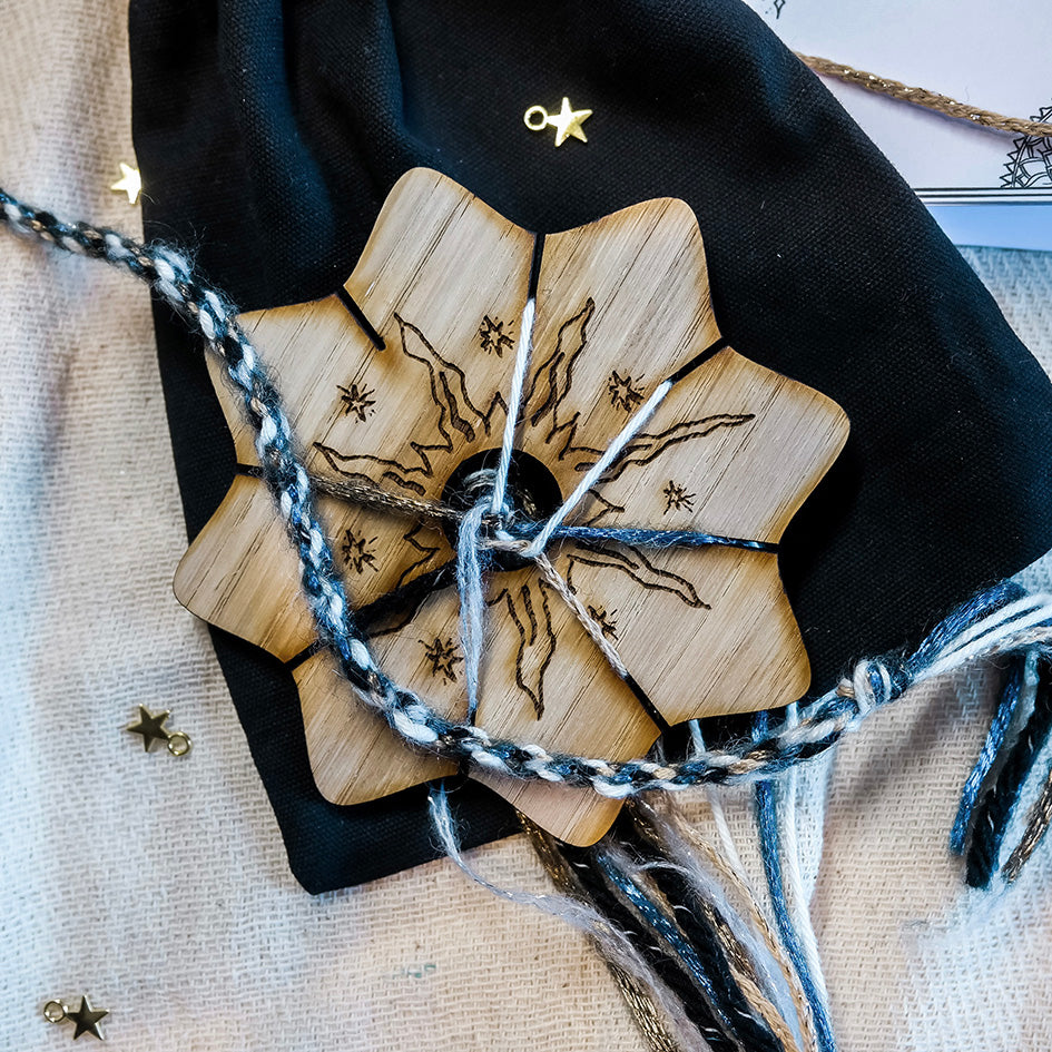 a wooden disc engraved with a celestial sun design. It is used for weaving wool cords. Shown with keepsake velvet bag and metal star charms 