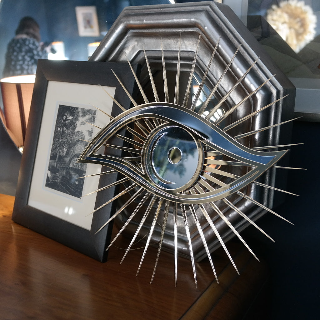 All seeing eye shaped mirror next to photo frames.