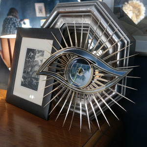 All seeing eye shaped mirror next to photo frames.