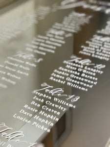 A white writing mirror seating plan for a wedding