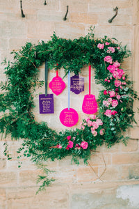 A purple and pink acrylic hanging seating plan display with wreath for a wedding