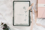 Load image into Gallery viewer,  handmade rag paper table number with floral design in frame with bow

