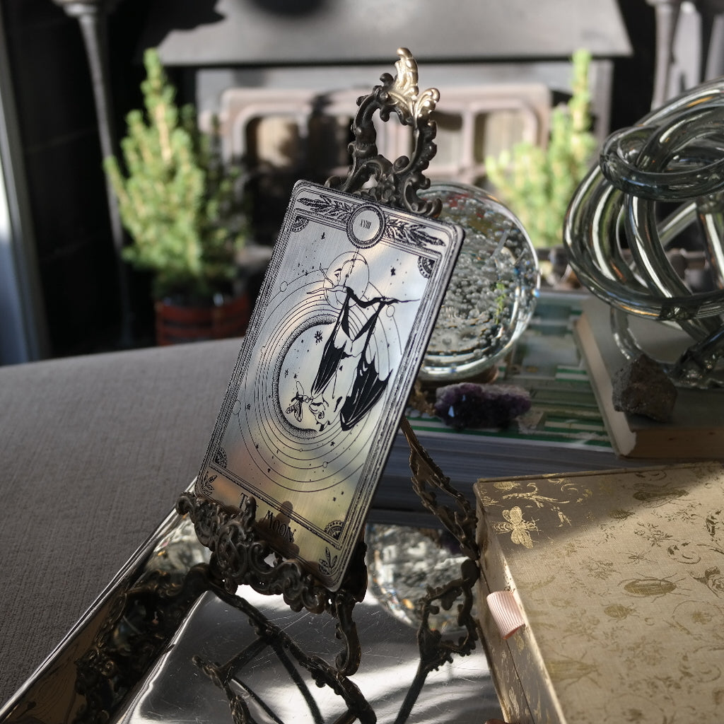 A decorative tarot card with a bat hanging under the moon on a stand.