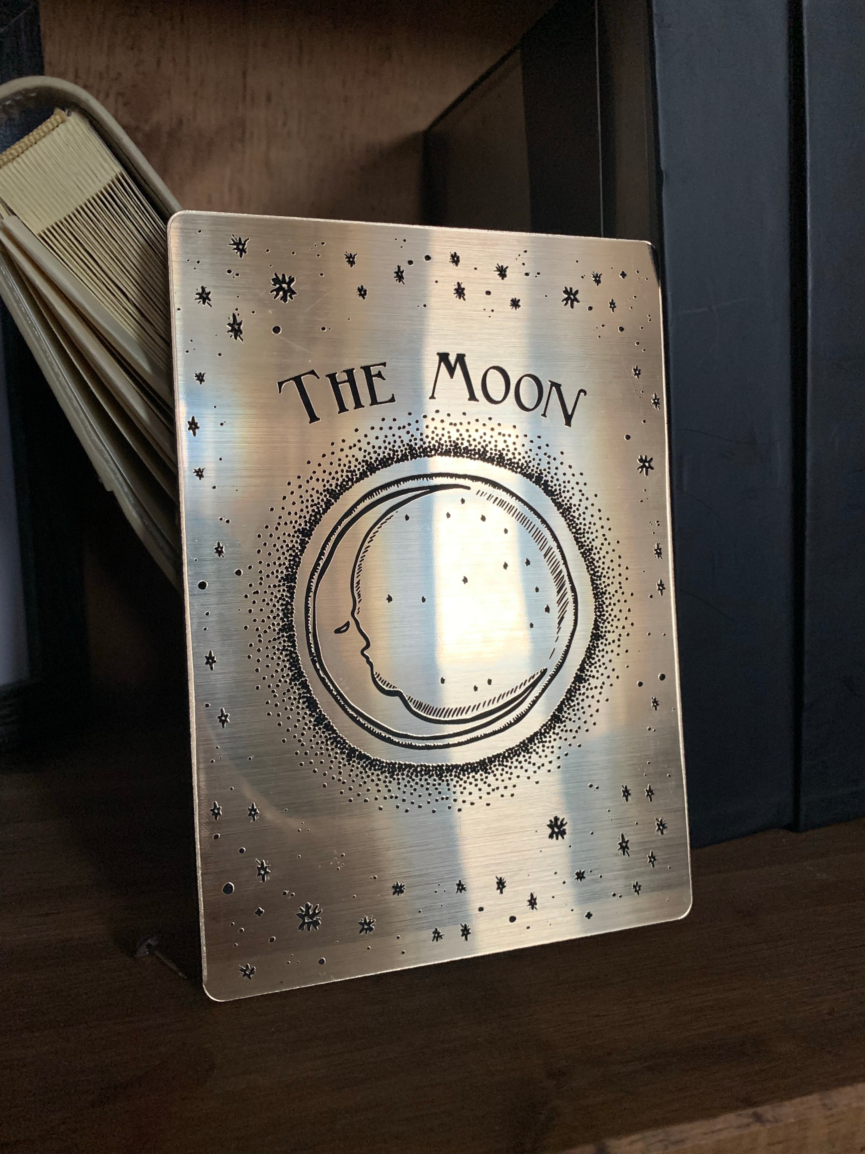 A gold decorative tarot card with etched design of a crescent moon, stars and the words 'the moon'