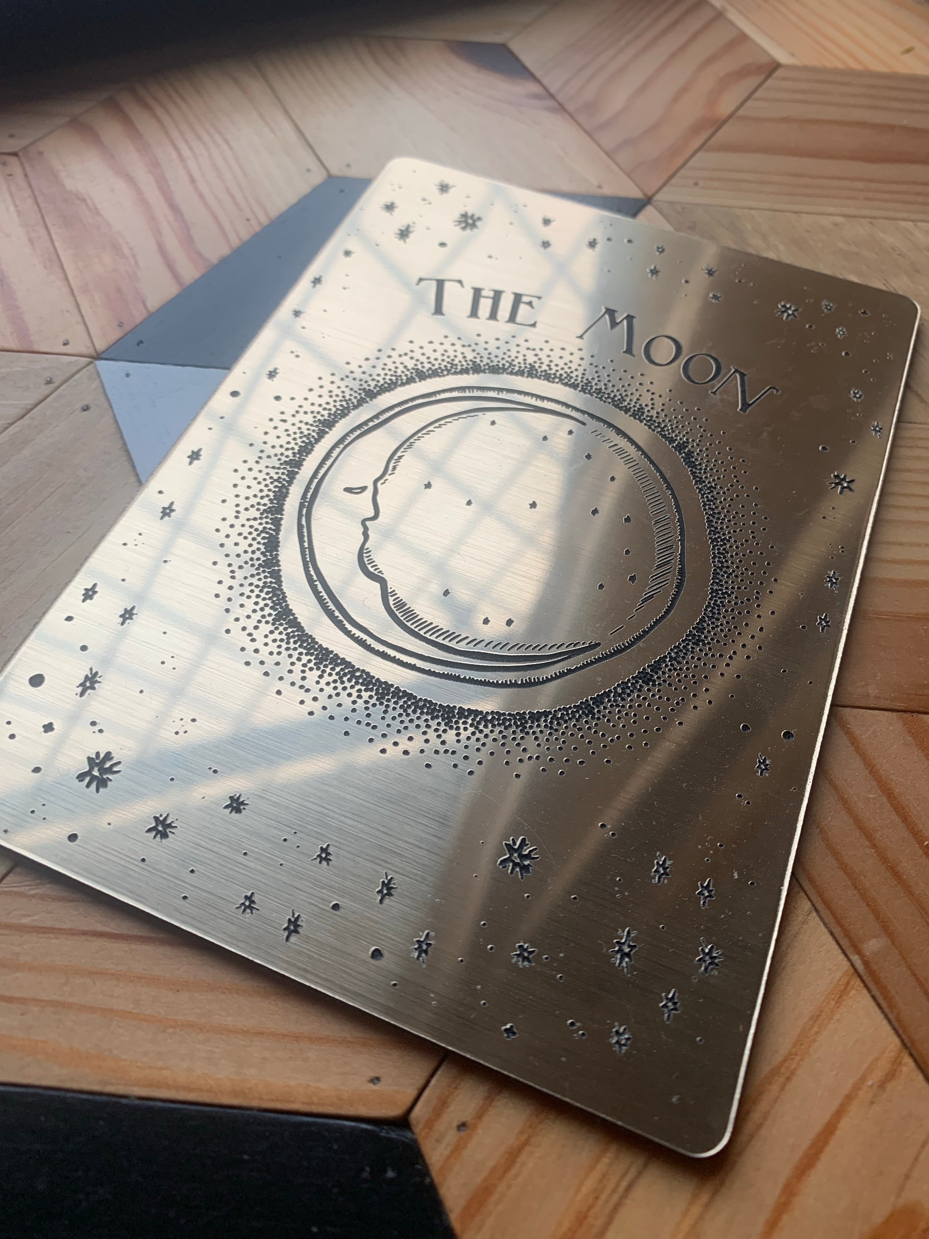 A decorative tarot card with etched design of a crescent moon, stars and the words 'the moon laying flat.